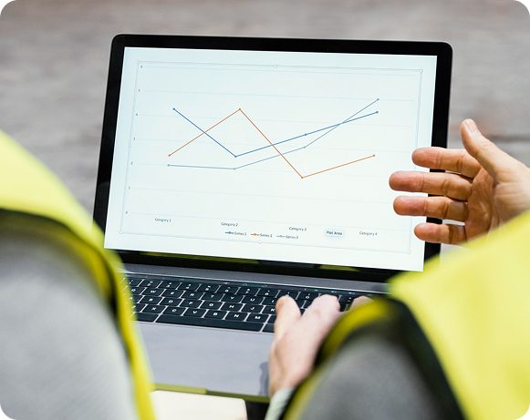 Man in a suit reviews documents while a woman with head in hand looks distressed. A laptop, coffee cup, folders, and a box are on the table. Bright room.